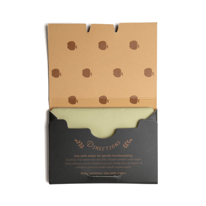 A packaged cleansing product shown open against a plain white background. The top flap is kraft brown with a repeating dark brown apple motif, and the lower section is black with the word 'Directions' printed in brown.
