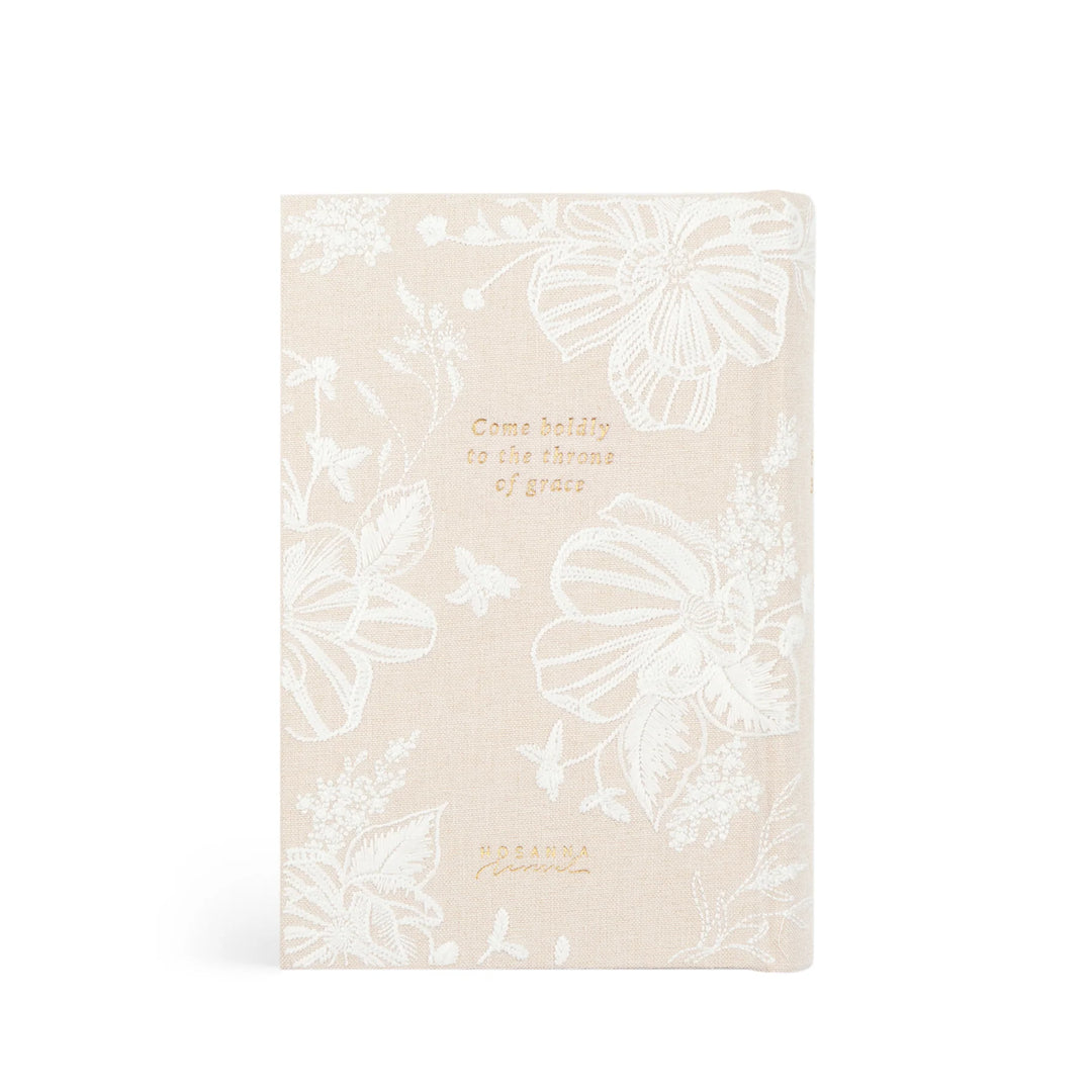 Beige Bible with white embroidered floral patterns and gold text on a white background