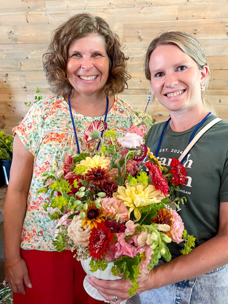 Two women holding a large bouquet of flowers against a wooden wall.