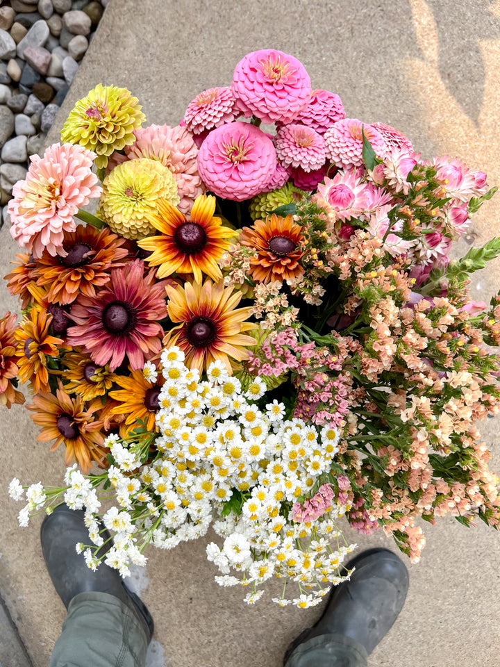 Bucket of colorful flowers including pink, yellow, and orange blooms on a stone surface.