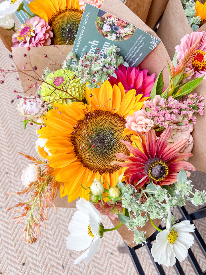 Bouquet of flowers with a sunflower and other colorful blooms on a textured surface.