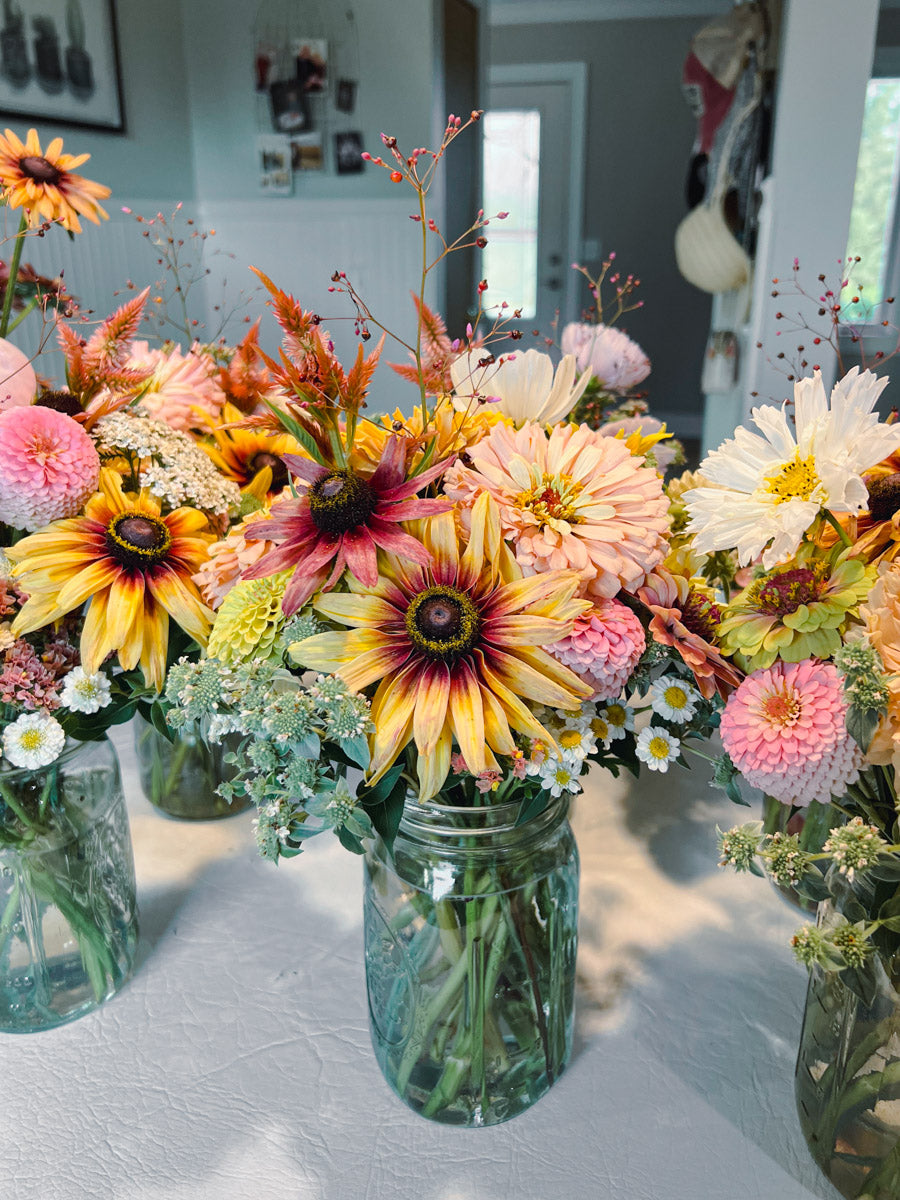 Colorful flower arrangements in mason jars on a table with a blurred indoor background
