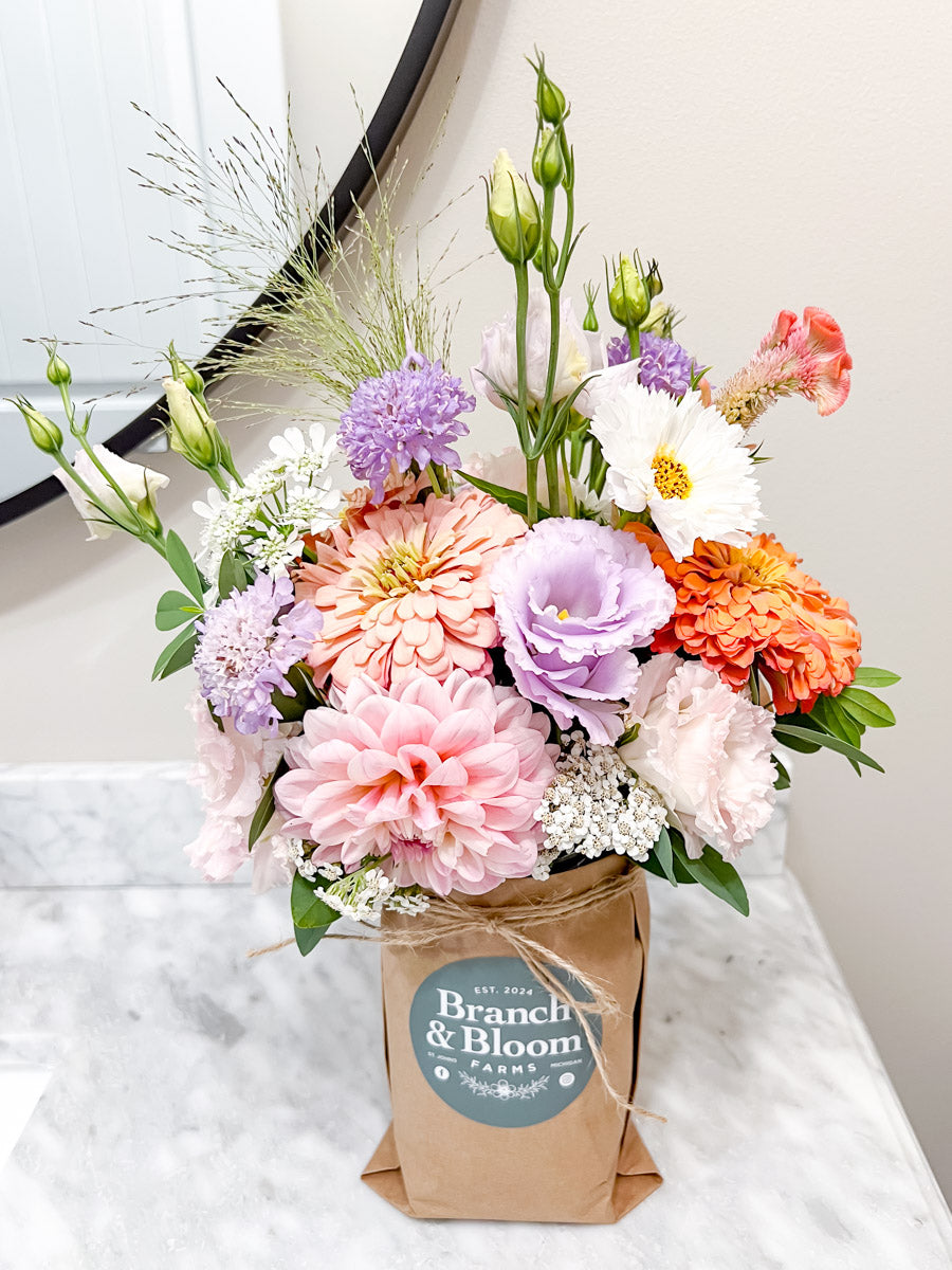 Colorful bouquet of flowers in a wrapped mason jar with 'Branch & Bloom Farms' label on a white surface.