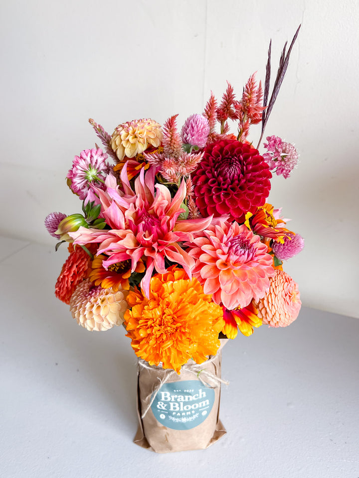 Bouquet of colorful flowers in a wrapped mason jar arrangement with 'Branch & Bloom Farms' branding on a white background.