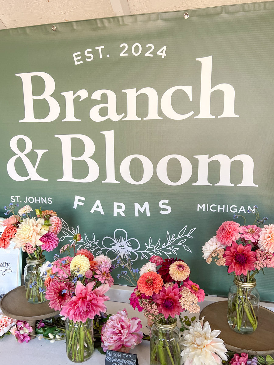 Floral arrangements displayed in front of a green chalkboard sign for Branch & Bloom Farms, St. Johns, Michigan.