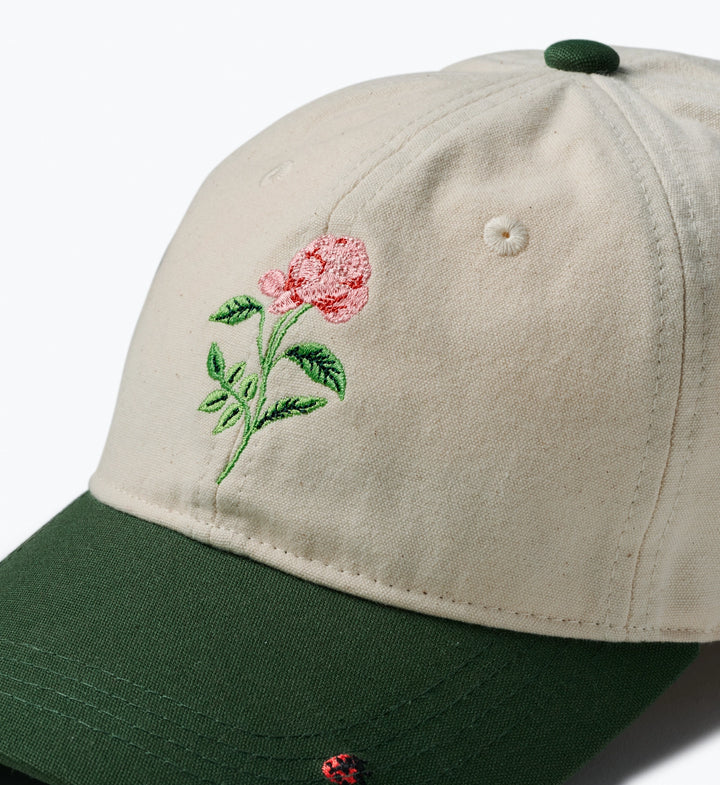Beige cap with green brim and embroidered pink flower on a white background