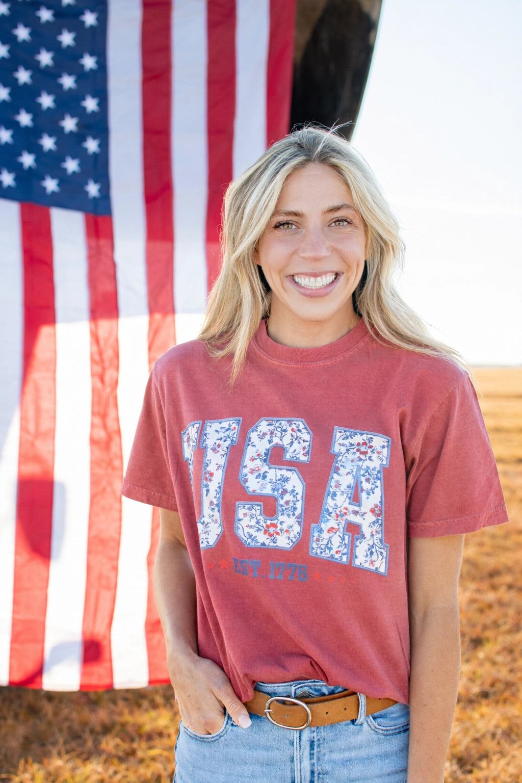 Woman wearing a red t-shirt with 'USA' printed on it in front of an American flag.