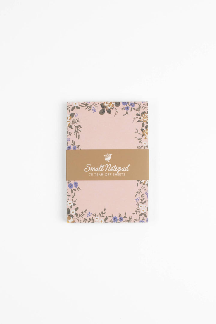 Small pink notebook with floral design and gold label on a white background
