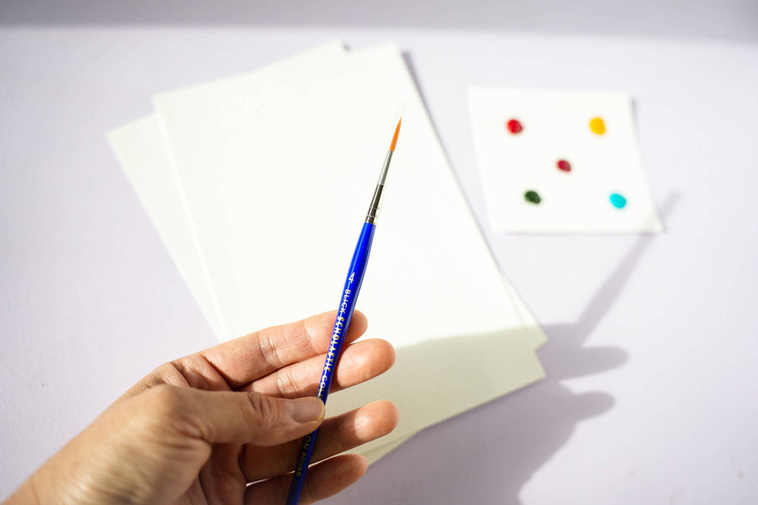 Hand holding a paintbrush with color swatches on a white background