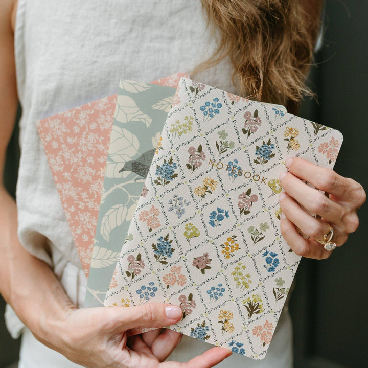 Person holding three patterned notebooks with floral designs.