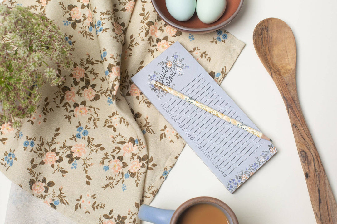 Notebook with floral design, wooden spoon, and mug on a floral cloth
