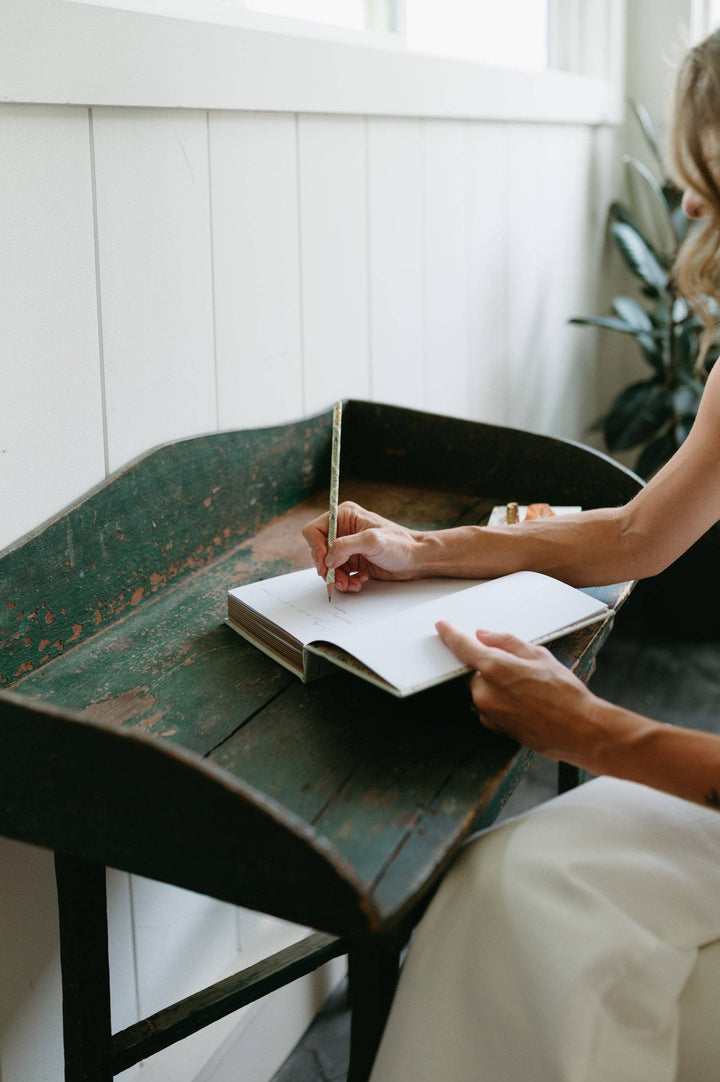 Person writing in a notebook on a rustic wooden table with a blurred background