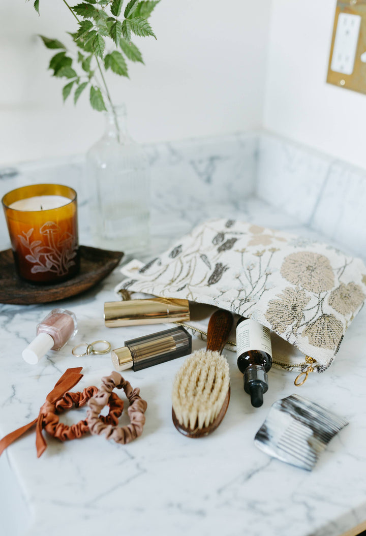 Personal care items including a candle, brush, and pouch on a marble surface.