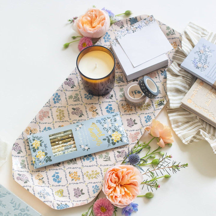 Table setting with floral tablecloth, candles, flowers, and stationery items.