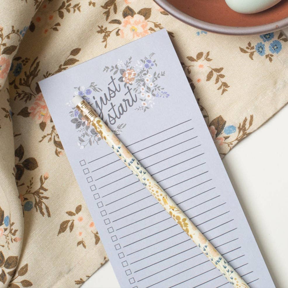 Notepad with floral design and pencil on a floral fabric background