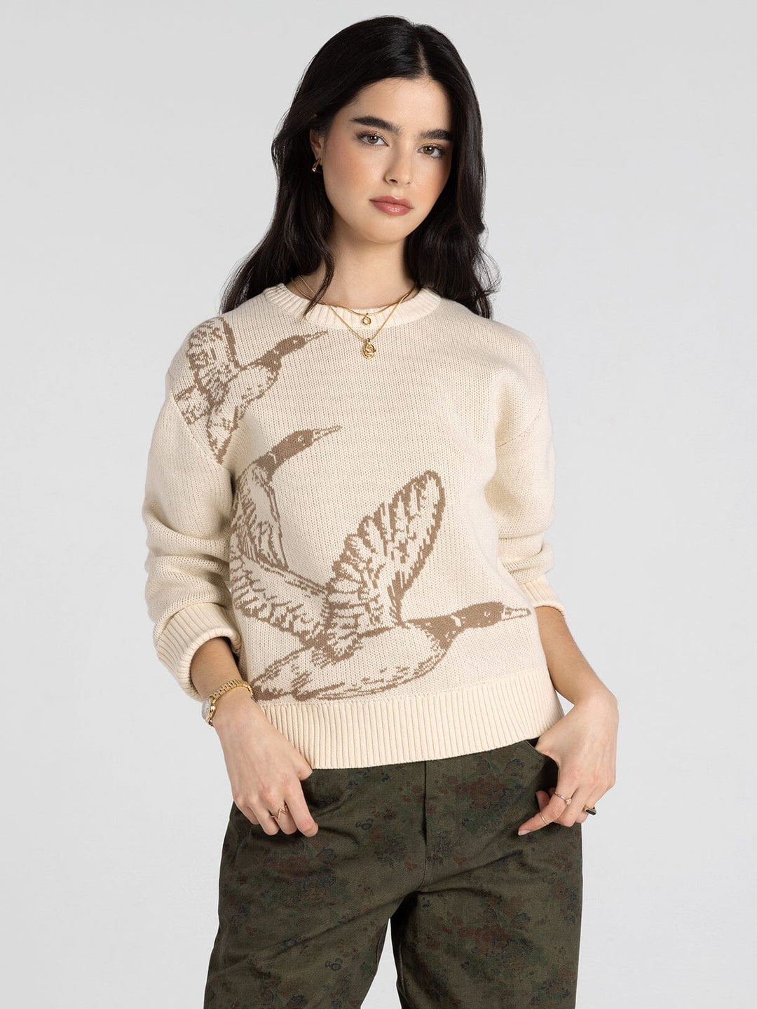 Woman wearing a beige sweater with mallard duck design on a plain background